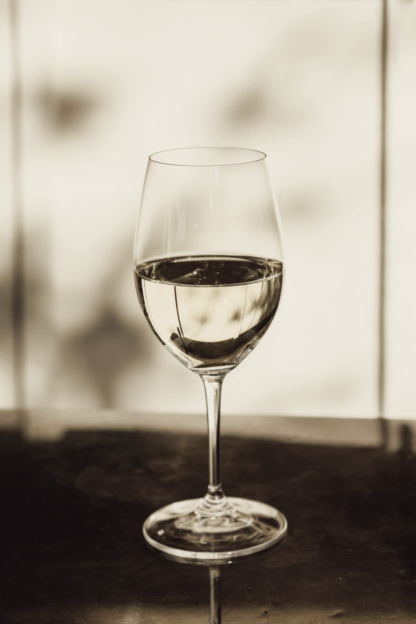 Un verre de vin blanc posé sur une table, dans la lumière d'une fenêtre