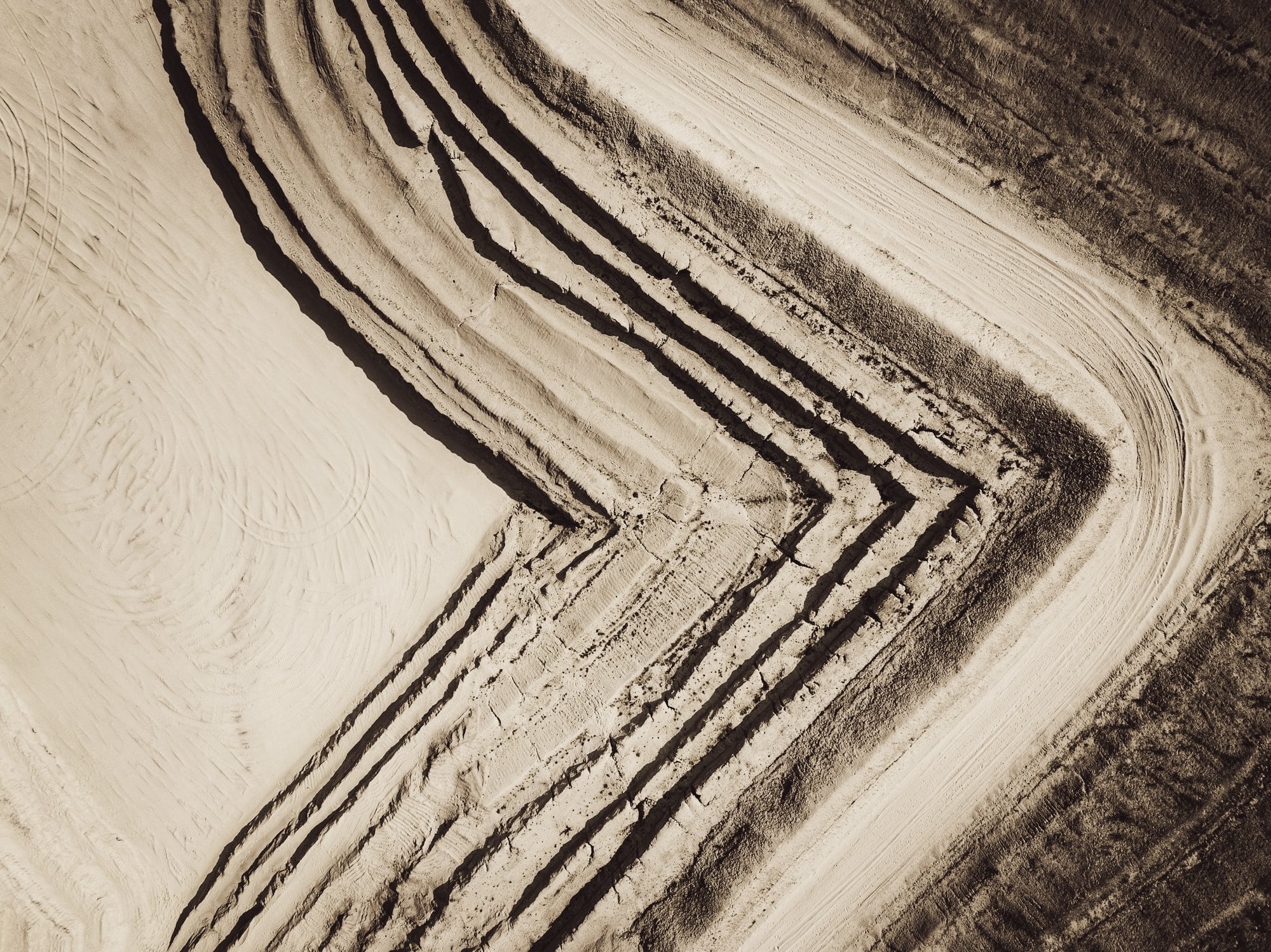 Vue aérienne d'une carrière : les strates de sable dessinent des chevrons clairs et sombres